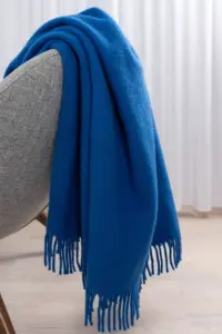 Kobaltblauwe wollen deken op een grijze bank met sierkussens – Blauwe woonaccessoires dé trend voor een eclectisch interieur goossenswonen.nl